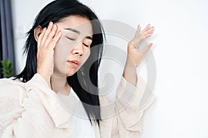 Asian woman having problem with Meniere`s disease, fainting or dizziness hand holding her head leaning against the wall photo