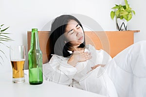 Asian woman having problems with GERD , acid reflux, and heartburn with gastritis from drinking beer before sleeping in bed