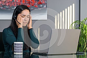 Asian woman having a stressful business call in headphones at a desk in home office