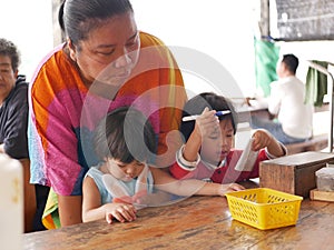 Asian woman helping two little girls sit properly, while they are eating out, at a dinning table at a restaurant