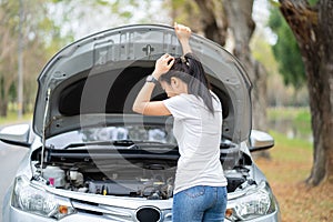 Asian woman beside her broken car. She opened the hood to see the damage. She touched her head with a hand in suspicion