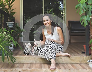 Asian woman and her two chihuahua dogs wearing dalmatian or cow patterned costume sitting on balcony with house plants, smiling
