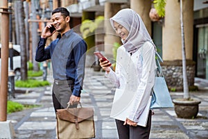 Asian woman in hijab using cell phone near businessman calling