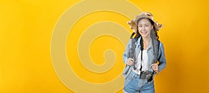 Asian woman hipster traveler with camera, backpack and hat in casual clothing happy and smiling over copy space yellow color backg