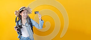 Asian woman hipster traveler with camera, backpack and hat showing credit card and smiling over copy space yellow color background