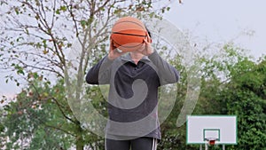 Asian woman holding basketball looking at camera at outdoor basketball playground.