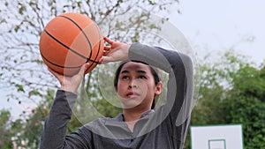 Asian woman holding basketball looking at camera at outdoor basketball playground.