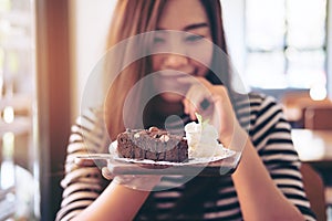 Asian woman holding brownie cake and whipped cream with feeling happy and good lifestyle in the modern cafe