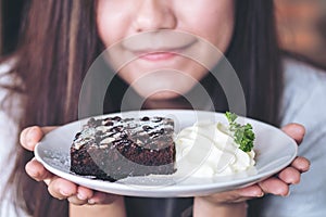 Asian woman holding brownie cake and whipped cream with feeling happy and good lifestyle in the modern cafe