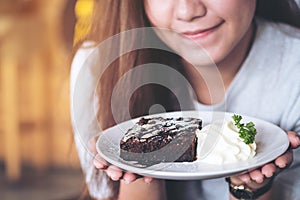 Asian woman holding brownie cake and whipped cream with feeling happy and good lifestyle in the modern cafe