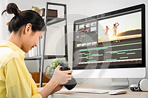 Asian woman holding a camera and using application video editor works on the computer.