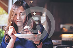 Asian woman holding chocolate cake roll and whipped cream and fork with feeling happy and enjoy eating in the modern loft cafe