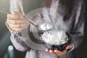 Asian woman holding cooked jasmine rice bowls with spoon. Wearing a gray sweater