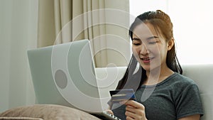 Asian woman holding a credit card for online shopping while sitting on the couch while on vacation at home