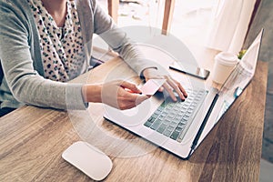 Asian woman holding credit card paying for shopping in computer laptop on wooden table