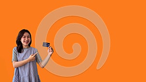 Asian woman holding credit card and thumbs up on orange background