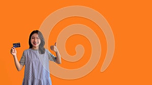 Asian woman holding credit card and thumbs up on orange background