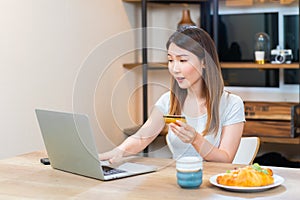Asian woman holding a credit card typing on keyboard for online shopping at home