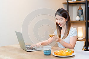 Asian woman holding a credit card typing on keyboard for online shopping at home