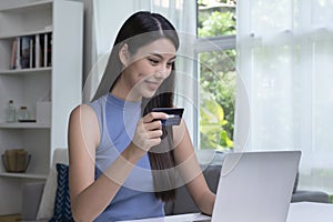 Asian woman holding credit card and using laptop computer. Businesswoman working at home. Online shopping, e-commerce, internet ba