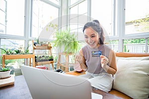 Asian woman is holding credit card and using smartphone shopping online at home. Online shopping, e-commerce, internet banking,