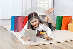 Asian woman holding credit card and  using tablet for online shopping  with colorful paper bag background