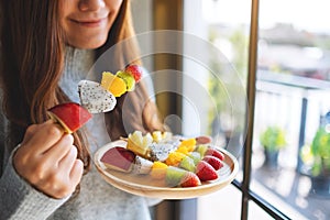 An asian woman holding and eating a fresh mixed fruits on skewers