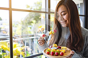 An asian woman holding and eating a fresh mixed fruits on skewers
