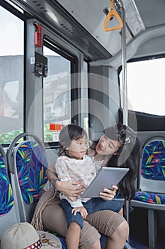 Asian woman is holding her daughter and showing tablet
