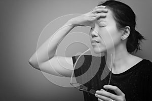 Asian woman holding her head, suffer from having a strong headache and fever, poor sight, farsightedness, myopia. black and white photo