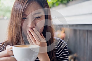 Asian woman holding hot coffee with feeling strange and smelling bad in coffee shop