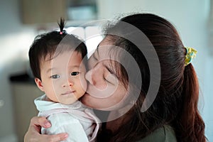 Asian woman holding and kissing on baby girl cheek.