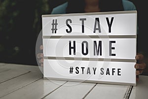 Asian woman holding a lightbox sign with text hashtag #STAY HOME and #STAY SAFE. COVID-19. Stay home save concept