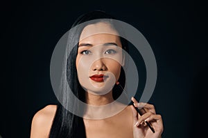 Asian woman holding lipstick over balck background