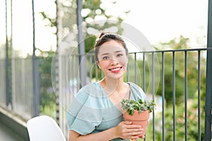 Asian woman holding and looking at plant potted on balcony at apartment in the morning