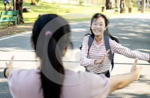 Asian woman holding opened arms and child girl daughter missed her mom running to mother standing in outdoor at primary school,
