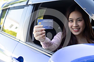 Asian woman holding payment card or credit card on the car.