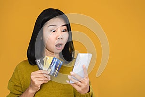 Asian woman holding smart phone and credit card shocked with overspending money from shopping online