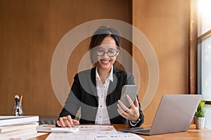 Asian woman holding smart phone while using calculator for business financial accounting calculate money bank loan rent