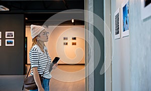 Asian woman holding tablet at art gallery collection in front framed paintings