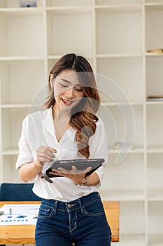 Asian woman holding a tablet standing in front of a desk, office worker concept