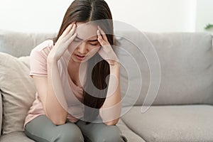 Asian woman are holding their hands to the head in pain on the sofa at home, Young women have severe headaches from migraines,