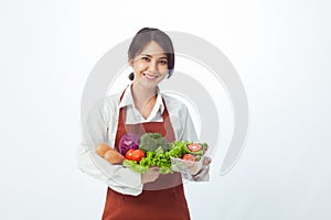 Asian woman holding vegetables and smiling on white background.