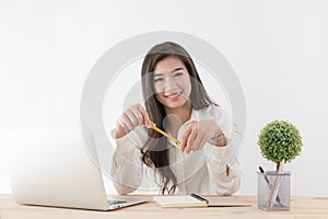 Asian woman holding yellow pencil in hand and using laptop,Female smiling happily working in a white office desk