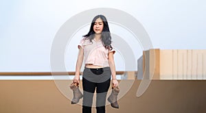 Asian woman holds brown boots in her hand and posting for photo shooting at rooftop environment at twilight time