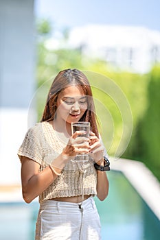 Asian Woman holds a glass of water from drinking at outdoor field with bokeh green banner background