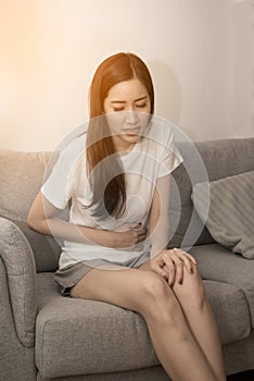 Asian woman holds her stomach with both hands. Stomach upset or pain during menstruation.