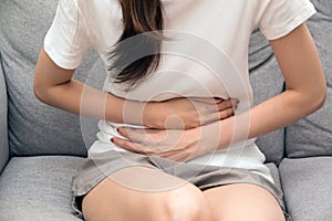Asian woman holds her stomach with both hands. Stomach upset or pain during menstruation.