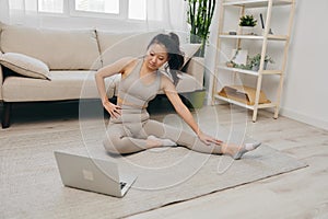 Asian woman at home exercising stretching and yoga repeating challenging exercises with video online watching on laptop