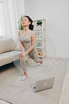 Asian woman at home exercising stretching and yoga repeating complex asanas and exercises online while looking at her